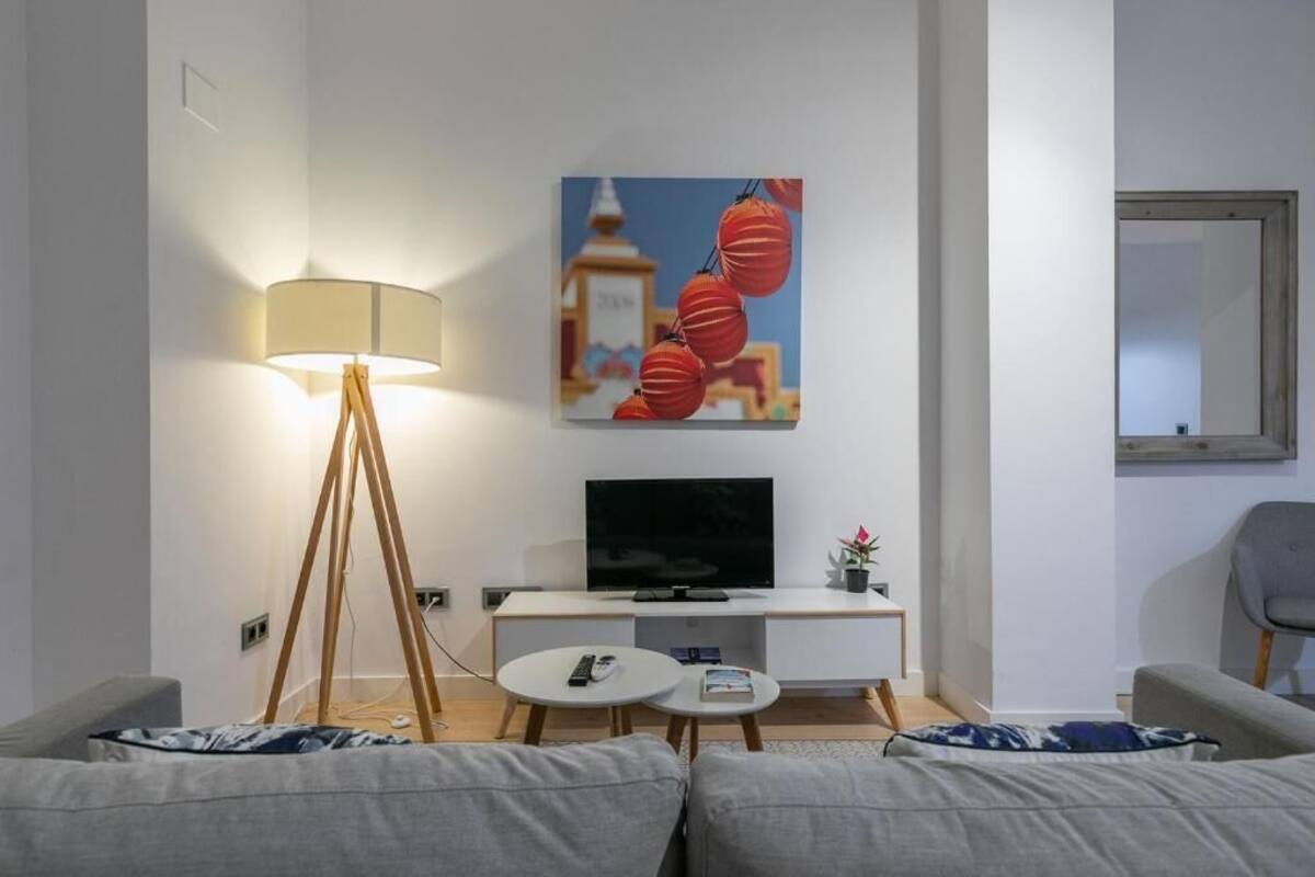Un salon moderne avec un canapé, une table basse, une lampe, un téléviseur à écran plat et un tableau représentant des lanternes rouges.