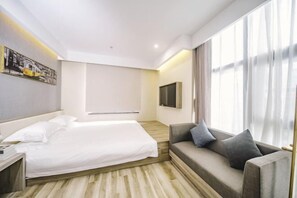 Habitación de hotel con cama, sofá, televisión de pantalla plana y un amplio ventanal con cortinas.