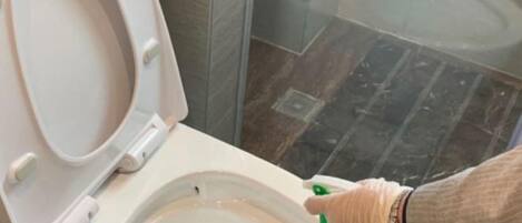 A person cleaning a toilet with a green spray bottle.