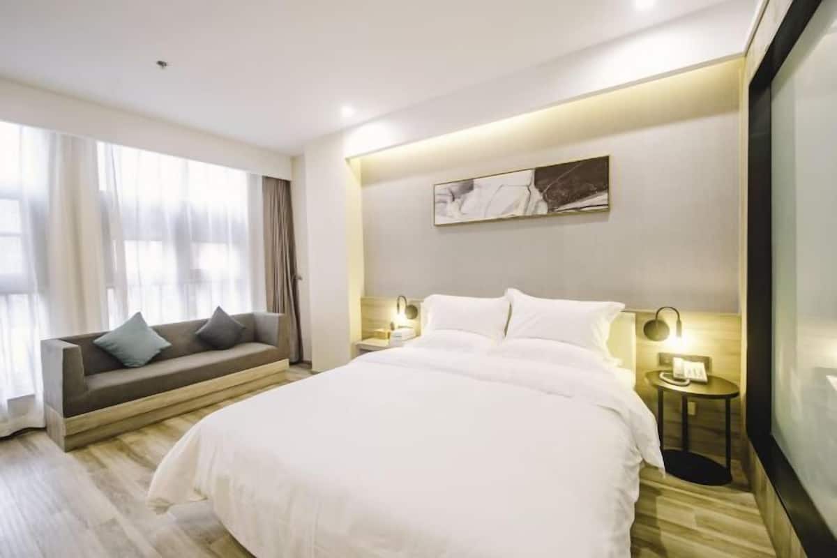 A modern hotel room with a large bed, a sofa, and two bedside tables with lamps.