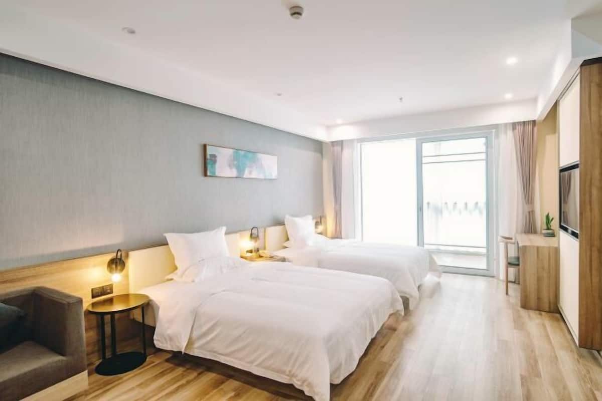 A hotel room with two beds, a desk, a chair, a small table, and a large window.