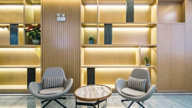 A modern interior with two armchairs and a round table, a wooden panel wall, and shelves with plants and decorative items. - Zhenjiang July hotel (Zhenjiang)