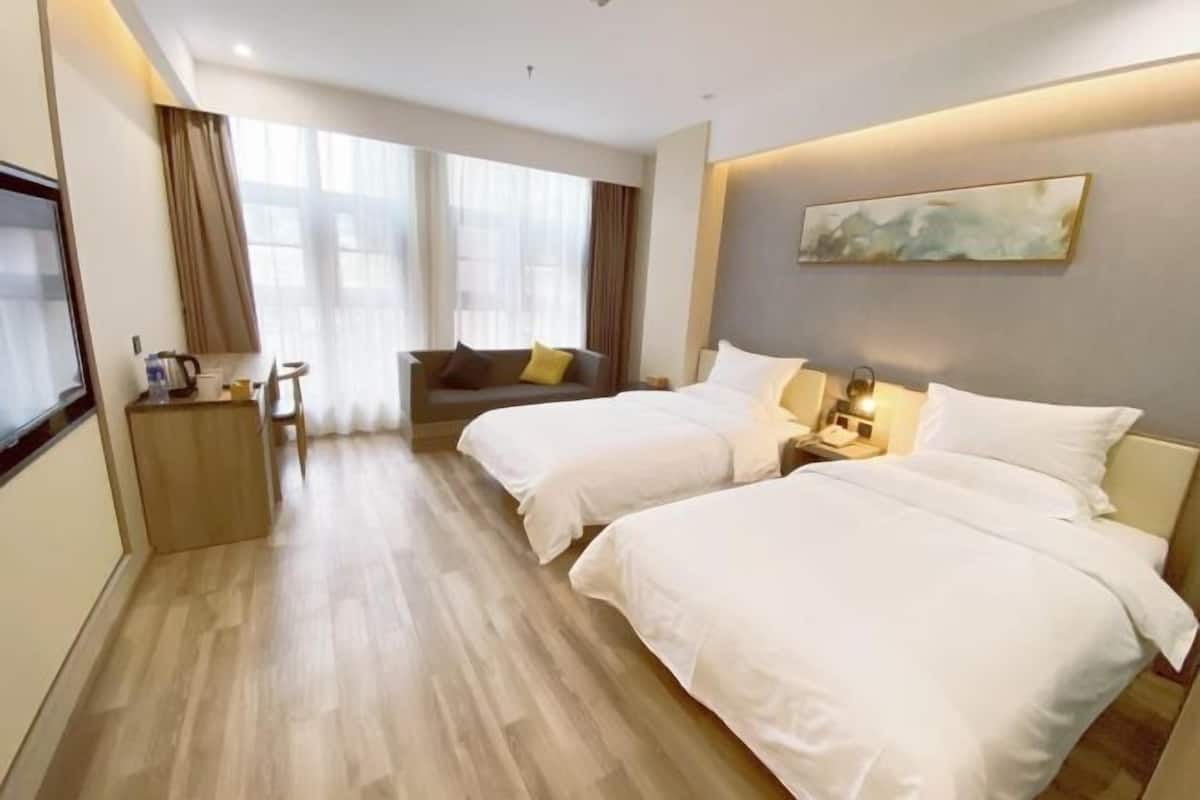 A hotel room with two beds, a sofa, a small table with a lamp, and a painting on the wall.
