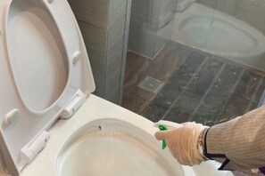 Un inodoro con la tapa cerrada, un rociador bidé portátil y un suelo de baldosas.