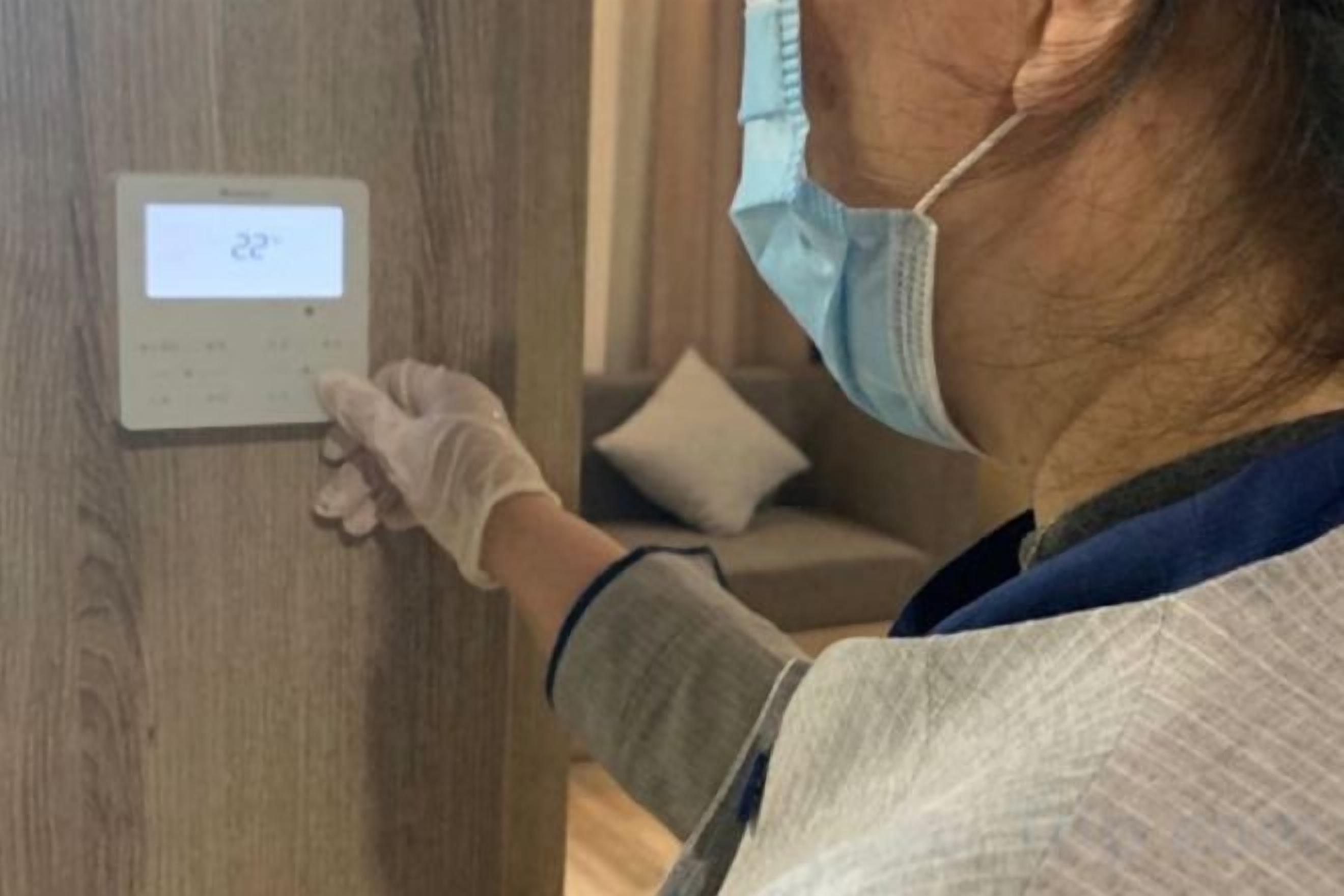 A person adjusting a thermostat on a wooden wall.