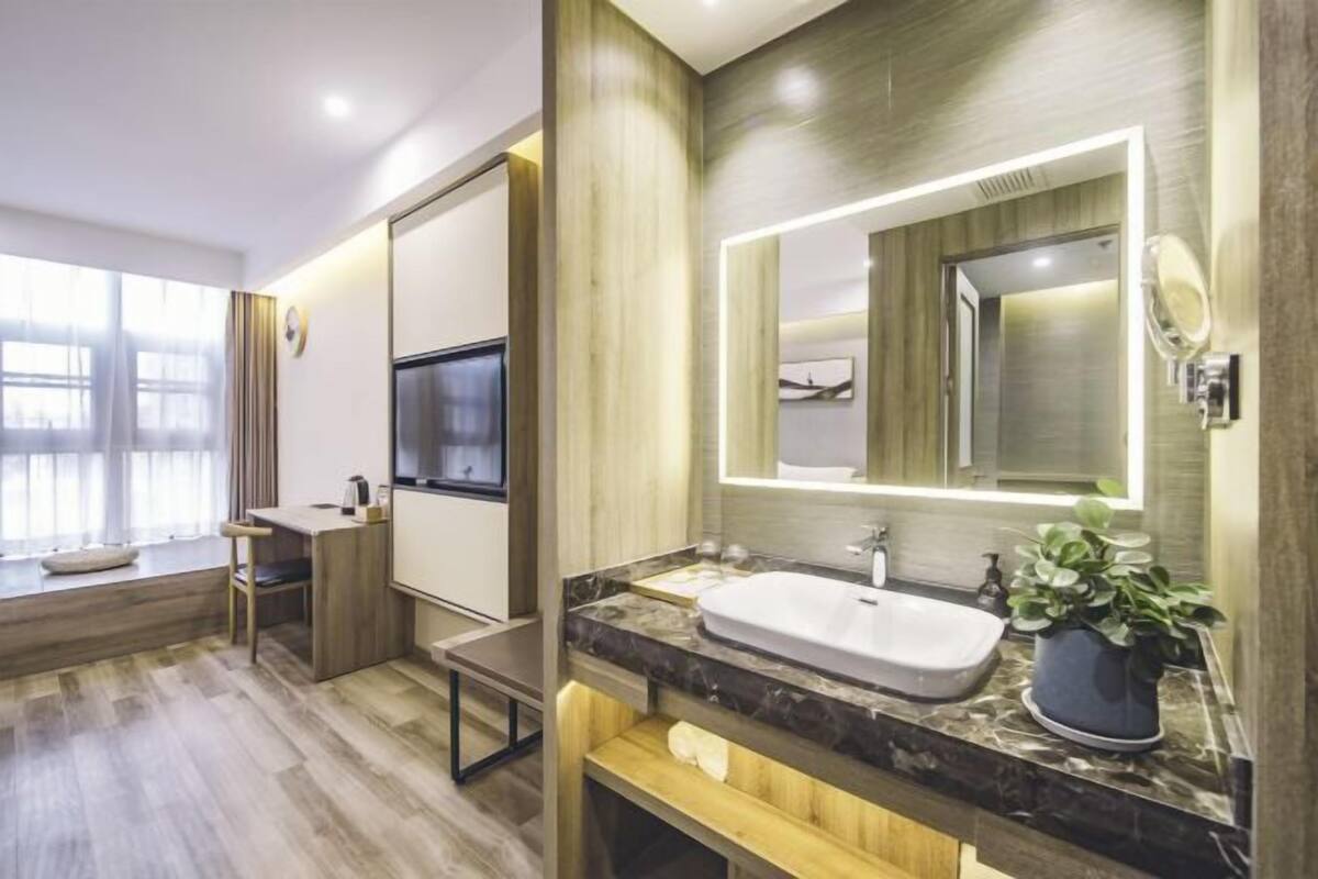 A modern bathroom with a large mirror, a sink, and a potted plant.