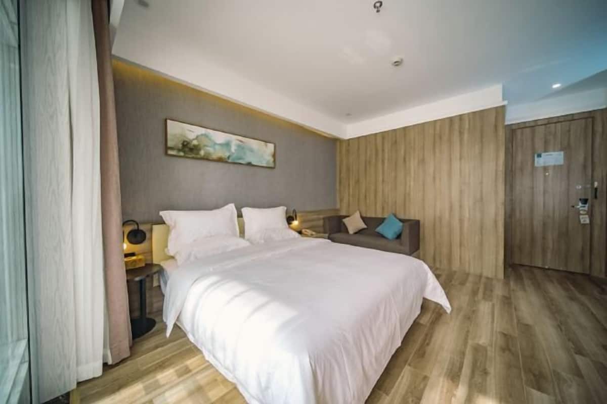 A hotel room with a large bed, a wooden wardrobe, a painting on the wall, and a nightstand with a lamp.