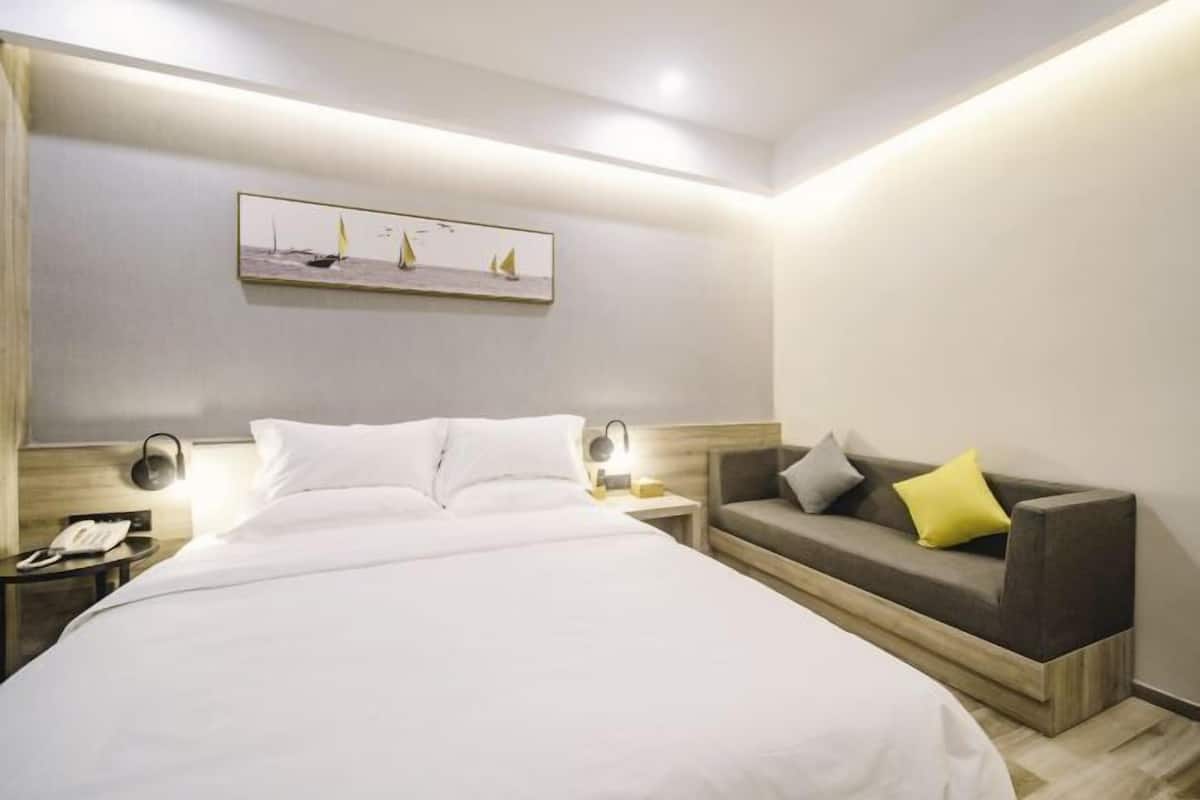 A hotel room with a bed, bedside table, lamp, and a sofa with cushions.
