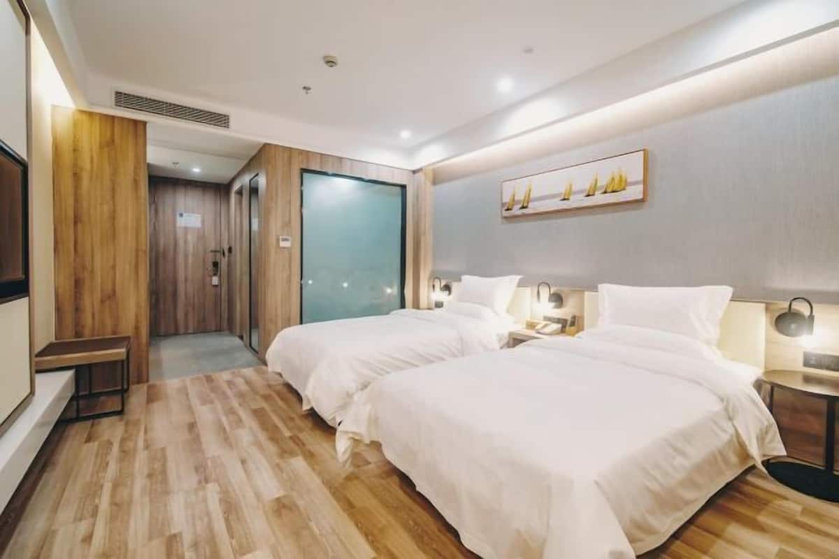 A hotel room with two beds, a wooden floor, a painting on the wall, and a TV on the left.