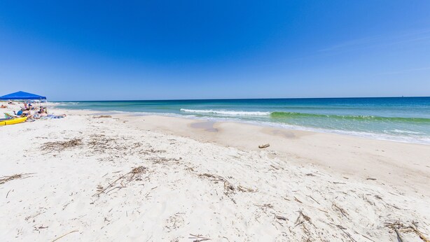 Ein Strand mit blauem Himmel, ruhigem Wasser und ein paar Personen in der Ferne.
