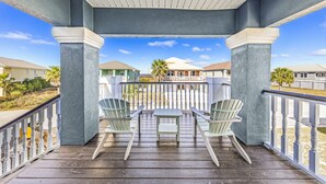 Ein überdachter Balkon mit zwei Adirondack-Stühlen und einem kleinen Tisch, mit Blick auf eine Wohngegend mit Häusern und einer Palme.