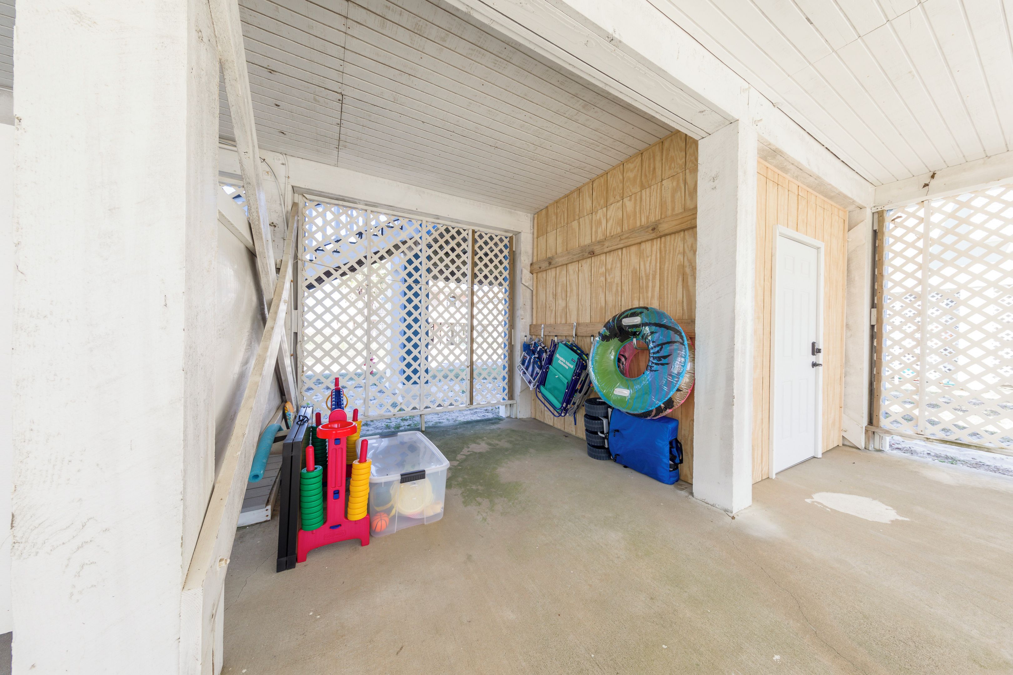 A covered outdoor area with a concrete floor, a wooden door, and a white lattice fence.