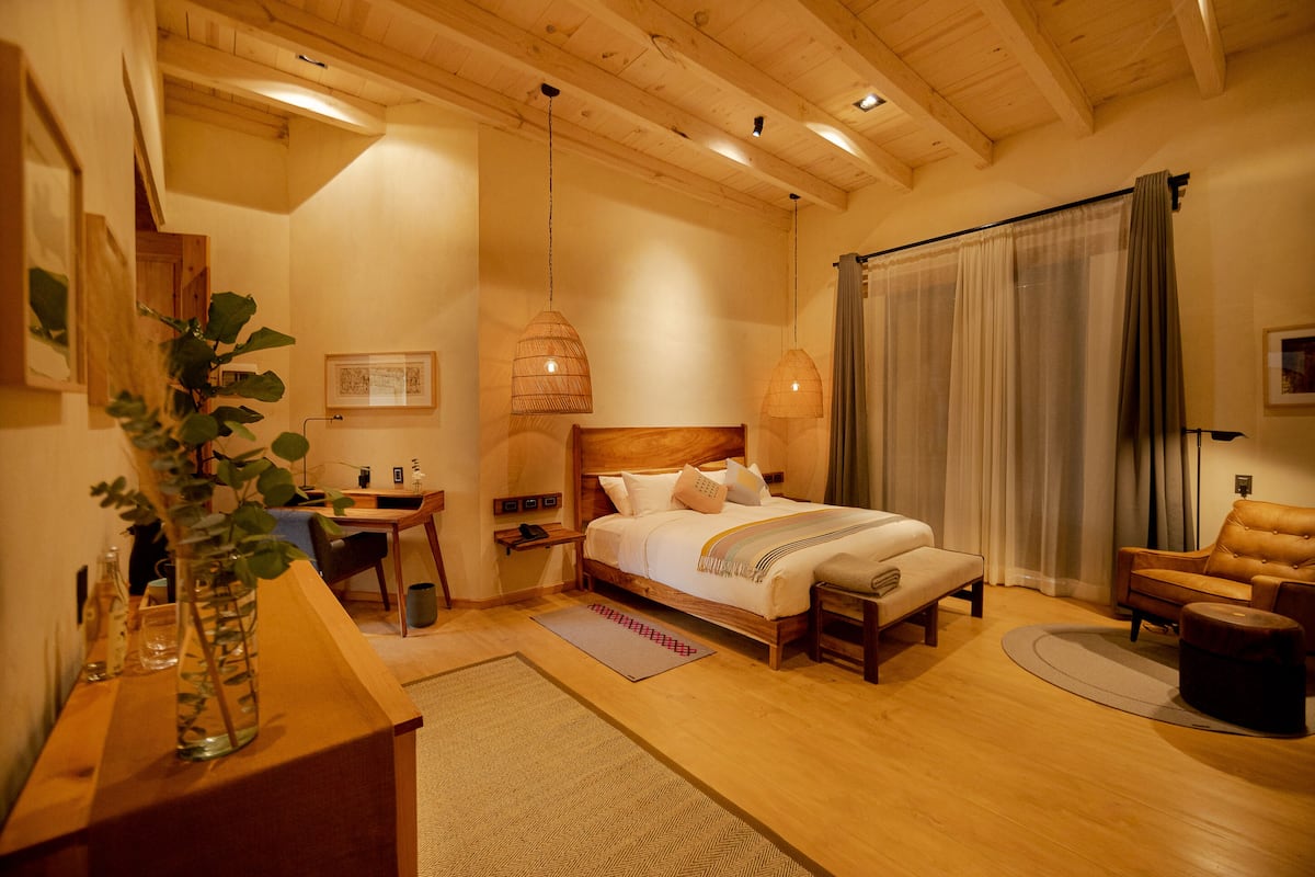 A well-lit bedroom with a wooden bed, bedside tables, a desk, and a chair.