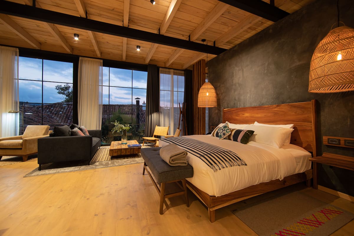A spacious bedroom with a large bed, wooden headboard, and a view of the outdoors through large windows.