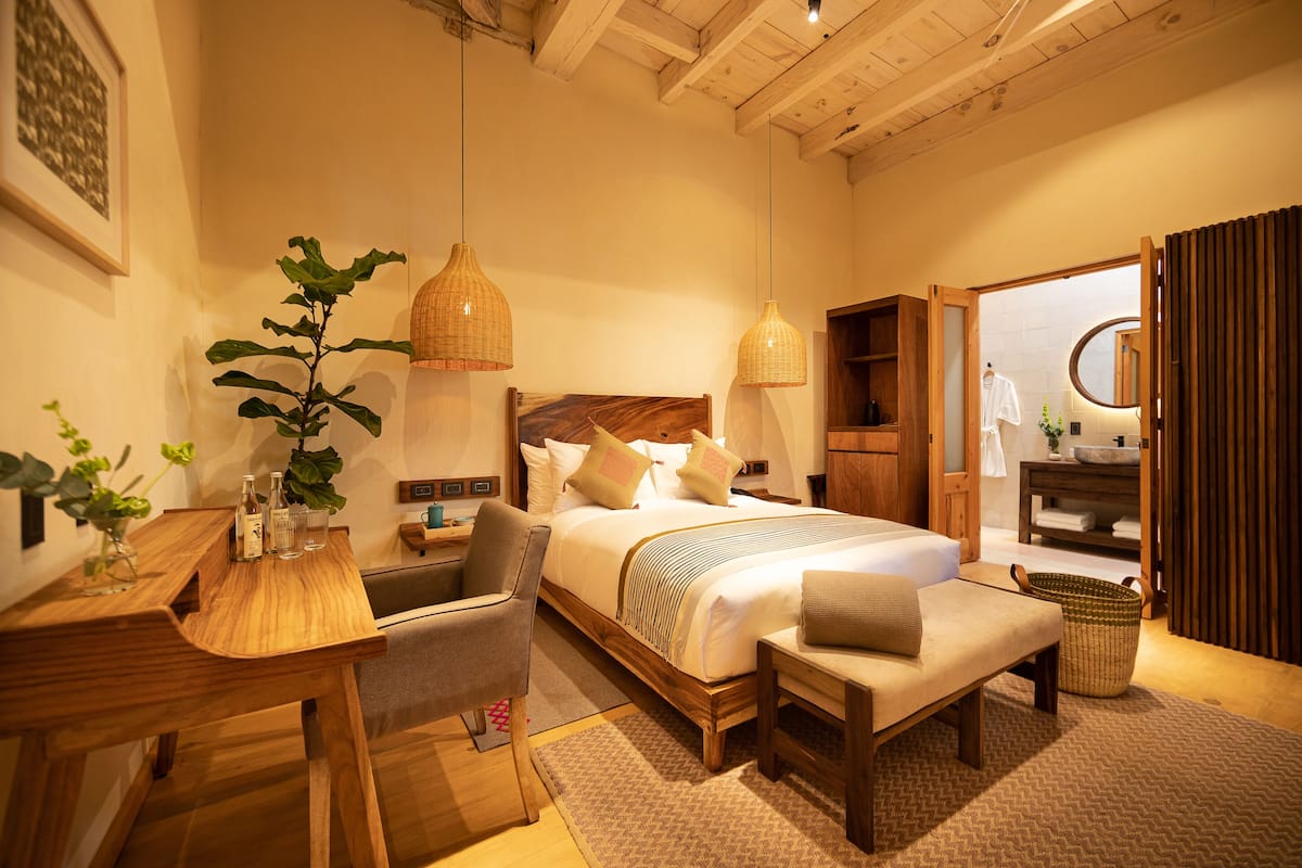 A well-lit bedroom with a wooden bed, bedside tables, a desk, and a chair.