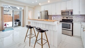 Una cocina moderna con armarios blancos, encimera de madera y electrodomésticos de acero inoxidable.