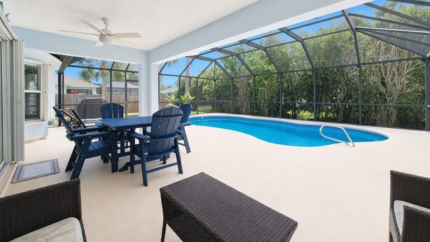 A covered outdoor area with a pool, a table with chairs, and a ceiling fan.