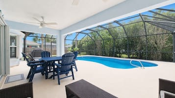 Un espace extérieur abrité comprenant une piscine, une table avec des chaises et un ventilateur de plafond.