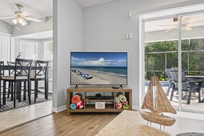 A living room with a television displaying a beach scene, a wooden entertainment unit with rolled-up rugs, and a sailboat decoration. - ☆☀︎❀ Tropical Paradise! Heated Pool, Boat Parking, Near Beaches! (Sebastian)