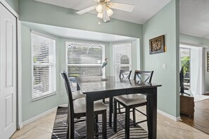 A dining area with a glass-top table, four chairs, and a ceiling fan.