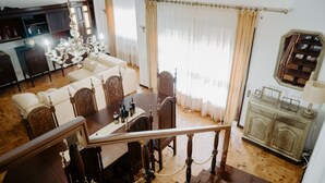 A dining area with a wooden table and chairs, a chandelier, and a view of the living room.