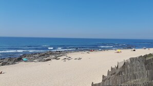 A beach with a wooden fence, rocky shoreline, and people relaxing.