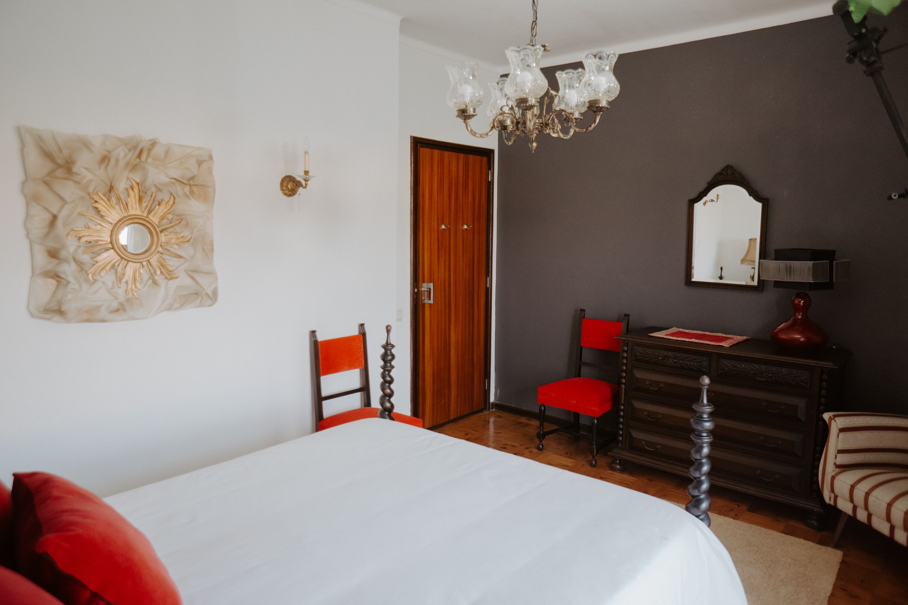 A bedroom with a bed, a dresser, a mirror, and a chandelier.