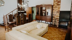 A living room with a beige sofa, wooden dining table, chairs, a wooden cabinet, a fireplace, and a TV.
