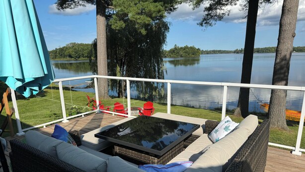 A deck with wicker furniture, a glass-top table, and red chairs.