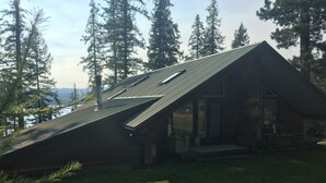 A cabin with a sloped roof, surrounded by tall trees and a view of a lake. - Lakefront home on McGregor Lake<br>Marion, Montana  (Marion)