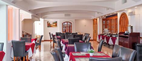 A dining area with tables set for service, a kitchen area with cooking equipment, and a view of the dining area through an arched doorway.
