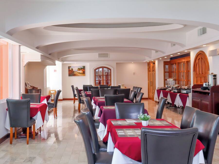 Uma área de refeições com mesas preparadas para o serviço, uma cozinha com equipamentos de culinária e vista para a área de refeições por uma porta arqueada.