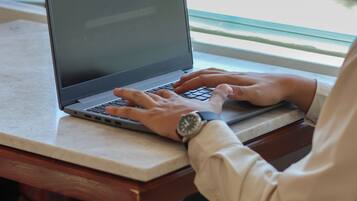 A person using a laptop on a wooden table with a plant in the background.