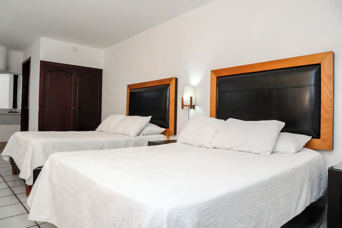 A hotel room with two beds, a wooden wardrobe, a nightstand, and a wall-mounted lamp.