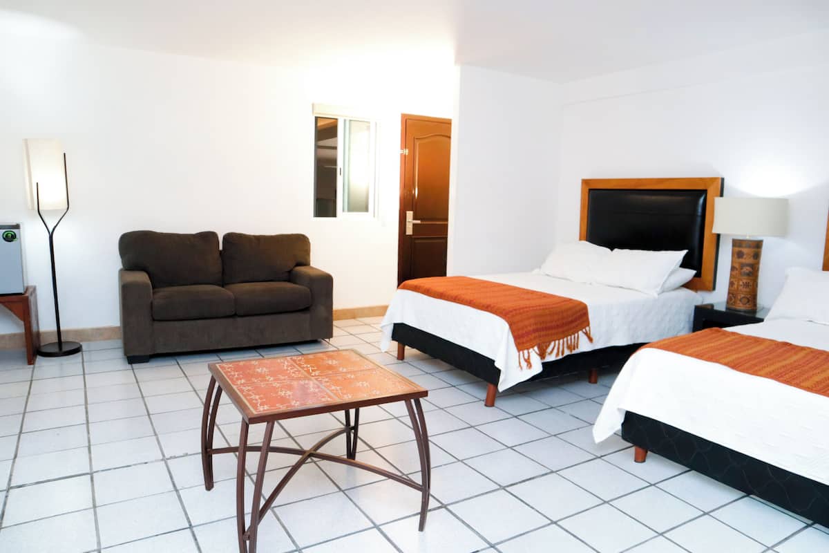 A hotel room with two beds, a sofa, a small table, and a lamp.