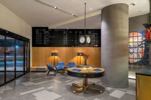 A modern hotel lobby with a check-in counter, seating area, and a flight information board.