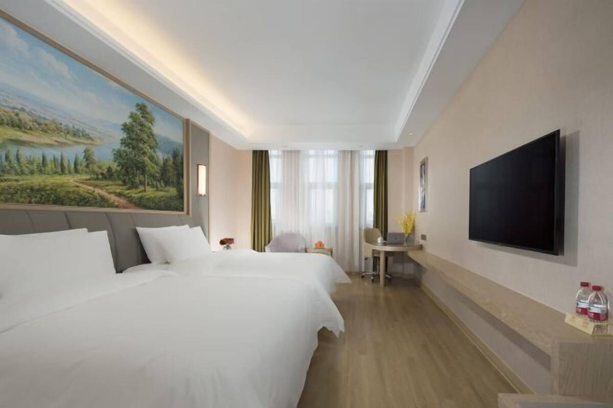 A hotel room with two beds, a desk with a chair, a flat-screen TV, and a painting on the wall.