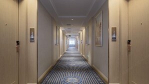Un long couloir étroit d’hôtel, avec un tapis à motifs, des portes des deux côtés et un plafond doté d’un éclairage encastré.