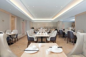 A hotel dining area with round tables, cushioned chairs, and a modern ceiling design. - Vienna International Hotel (Tianjin Meijiang Convention and Exhibition Center) (Tianjin)