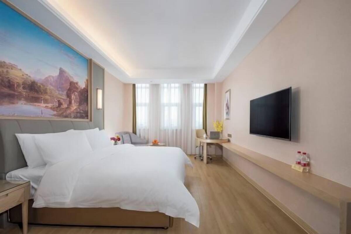 A hotel room with a bed, a desk, a chair, a TV, and a painting on the wall.