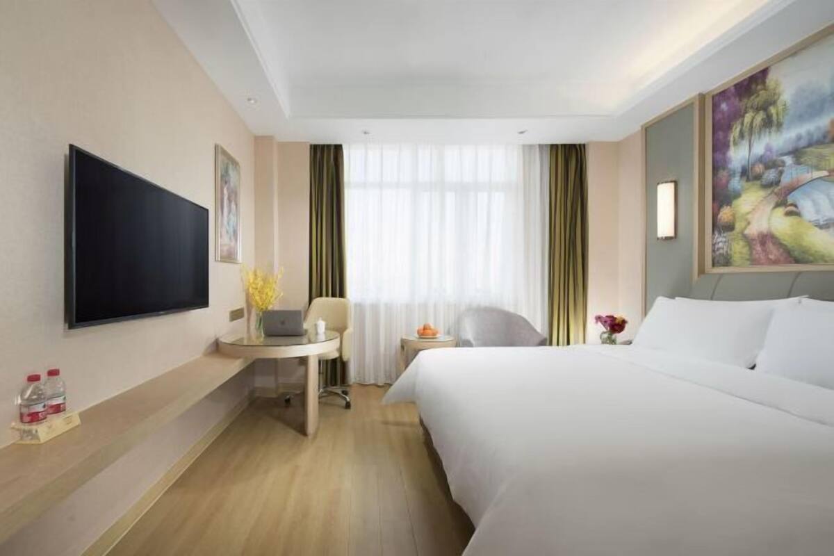 A hotel room with a bed, a desk, a chair, a television, and a window with curtains.