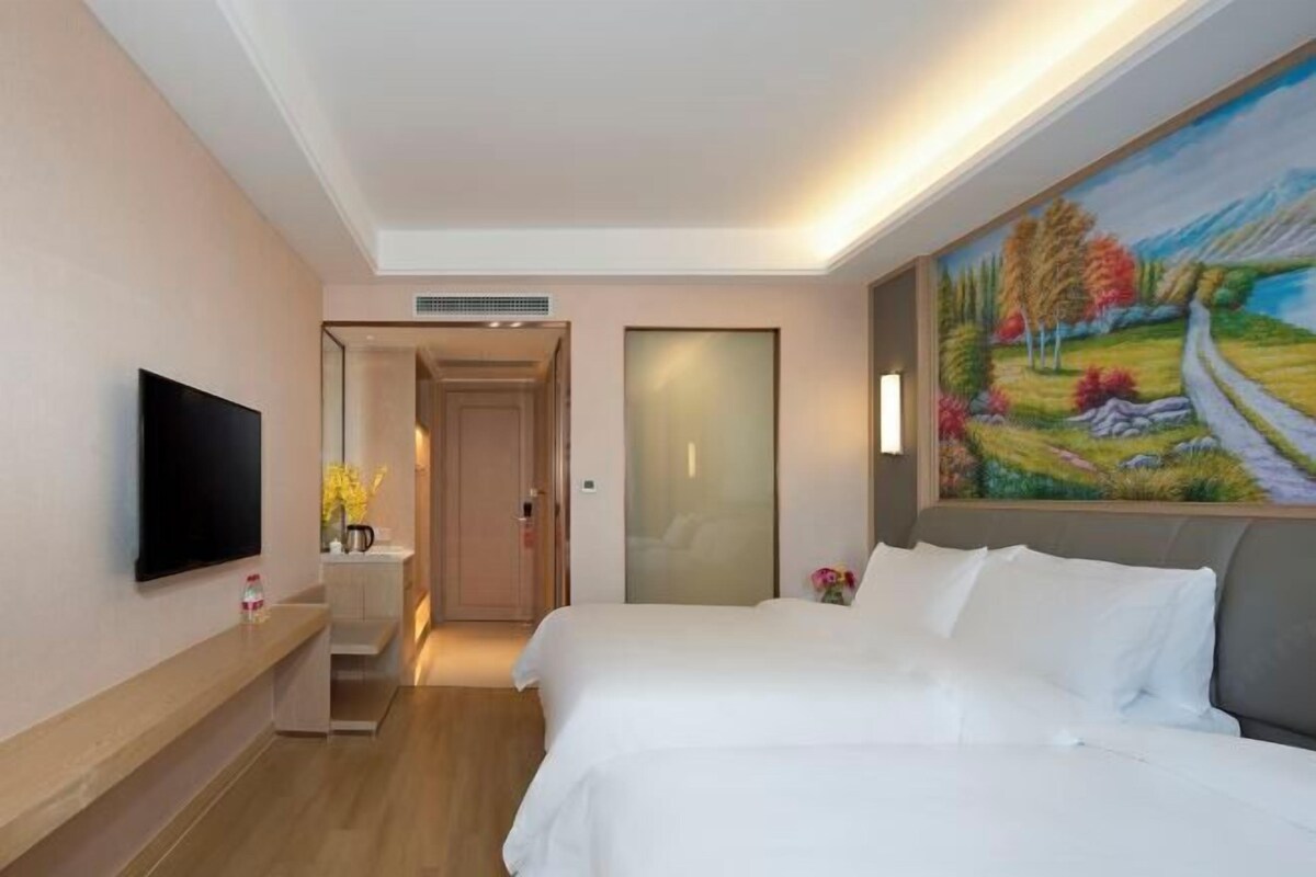 A hotel room with a bed, a TV, a painting, and a door leading to a bathroom.
