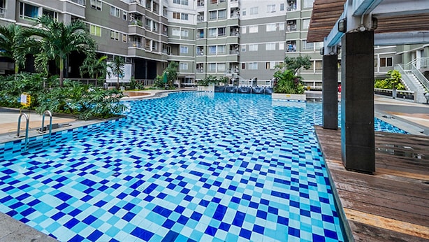 A swimming pool with blue and white tiles, surrounded by a wooden deck and greenery. - Prime Location Sudirman Park Studio Apartment (Jakarta)