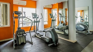 A gym with various exercise equipment, large windows, and orange walls. - Prime Location Sudirman Park Studio Apartment (Jakarta)