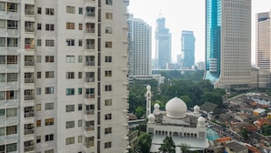 A high-rise residential building with multiple balconies and a mosque with domes in the foreground. - Prime Location Sudirman Park Studio Apartment (Jakarta)