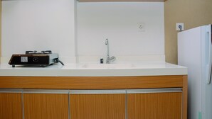 A kitchen with a white countertop, wooden cabinets, a sink, and a built-in range hood. - Cozy and Modern Signature Park Grande Studio Apartment (Jakarta)