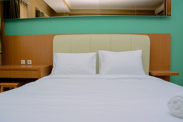 A neatly made bed with white linens, a wooden headboard, and a green wall.