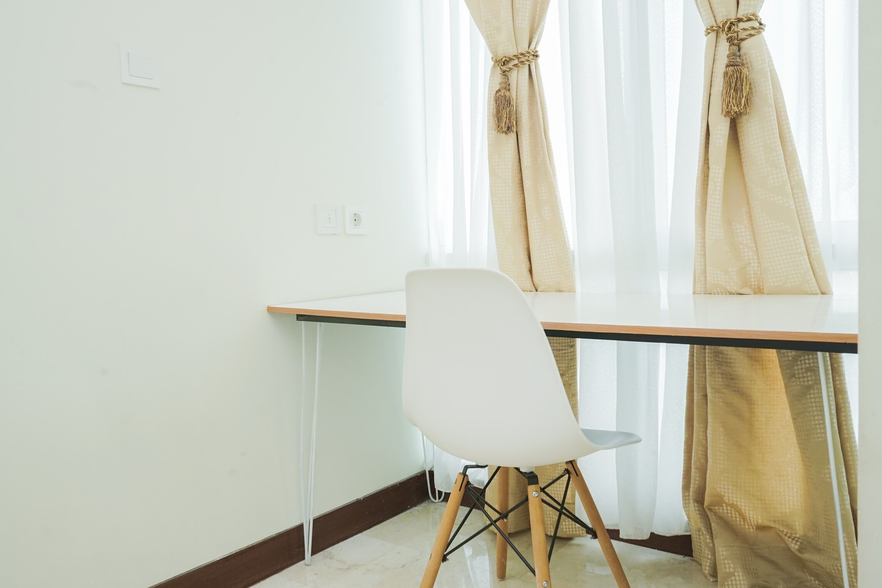 Ein Zimmer mit weißem Sessel, einem Holztisch und beigefarbenen Vorhängen mit Quasten.