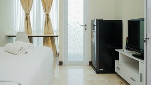 Een hotelkamer met een bed, een televisie, een koelkast en een raam met gordijnen.