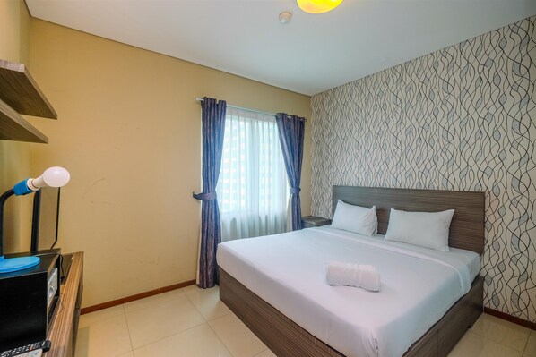 A hotel room with a bed, a bedside table, a lamp, and a window with curtains.